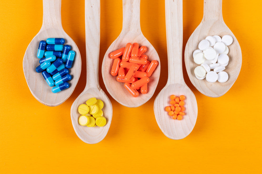 Cucharas de madera con cápsulas y comprimidos de colores sobre fondo naranja, representando micronutrientes esenciales