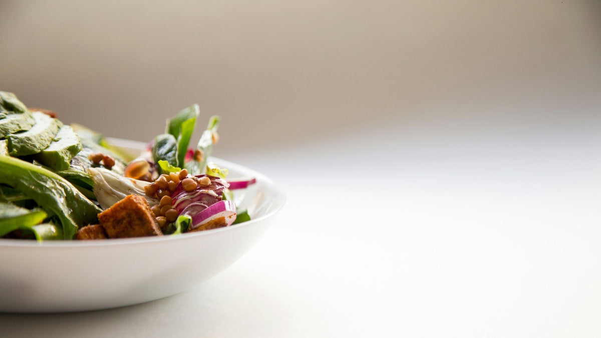 Primer plano de un plato de ensalada fresca con hojas verdes, lentejas, cebolla morada y croutones, que representa una alimentación basada en plantas