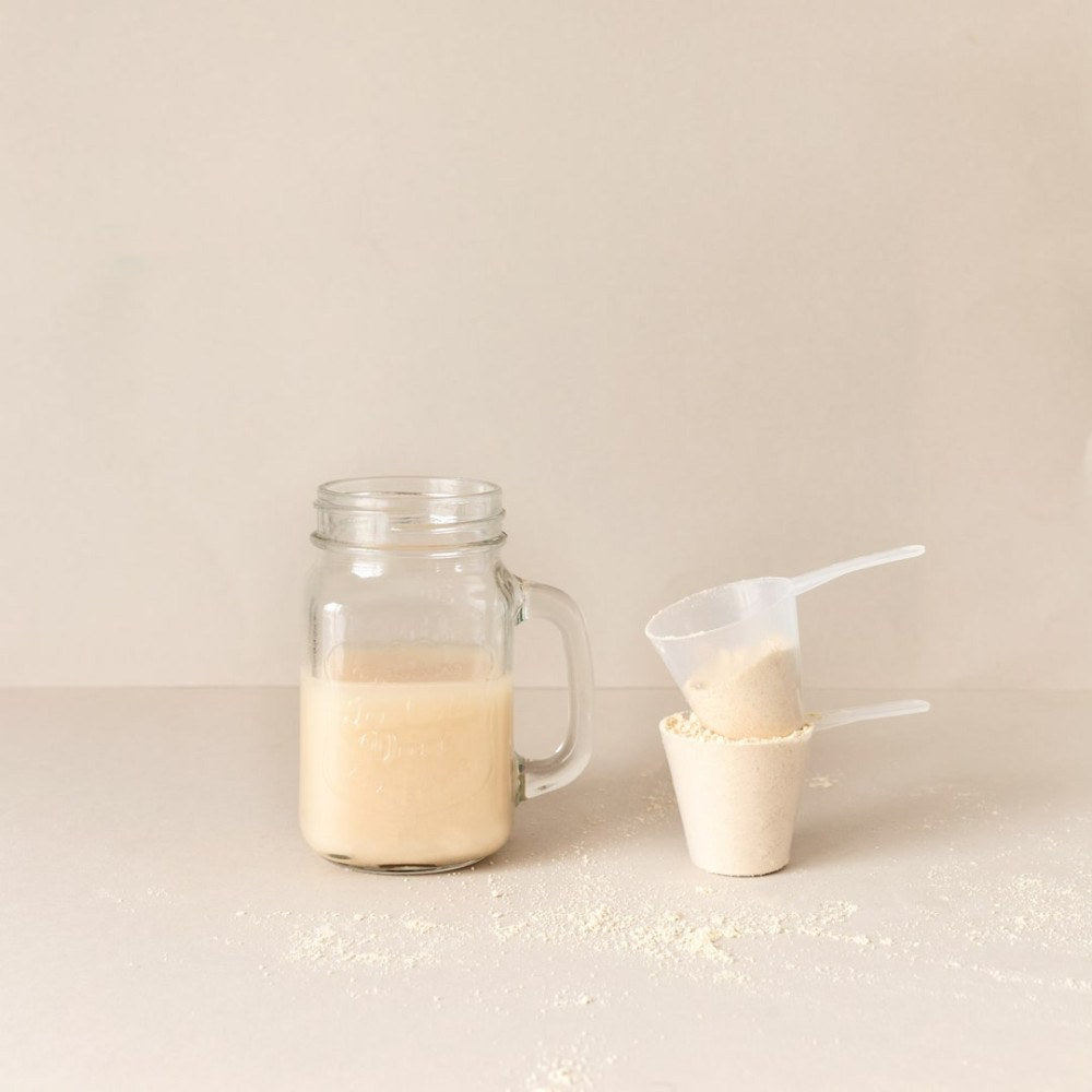 Satislent Complete Protein shake in a glass next to a scoop of powder