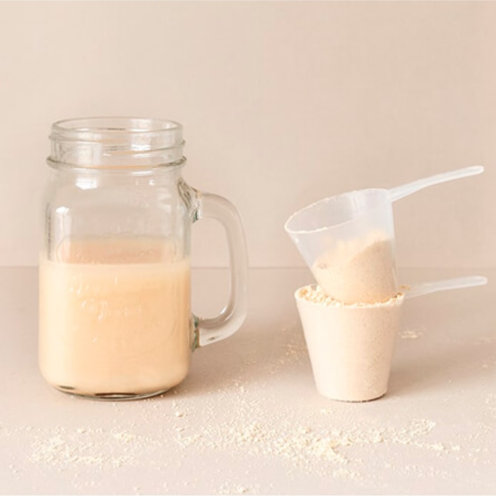 Satislent shake served in a glass next to two scoops of powder