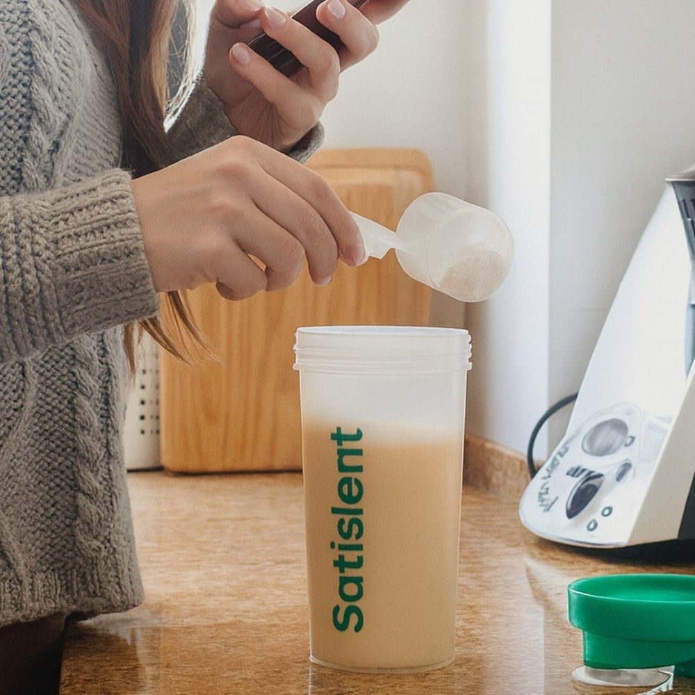 Adding a scoop of Satislent to the shaker on the kitchen counter