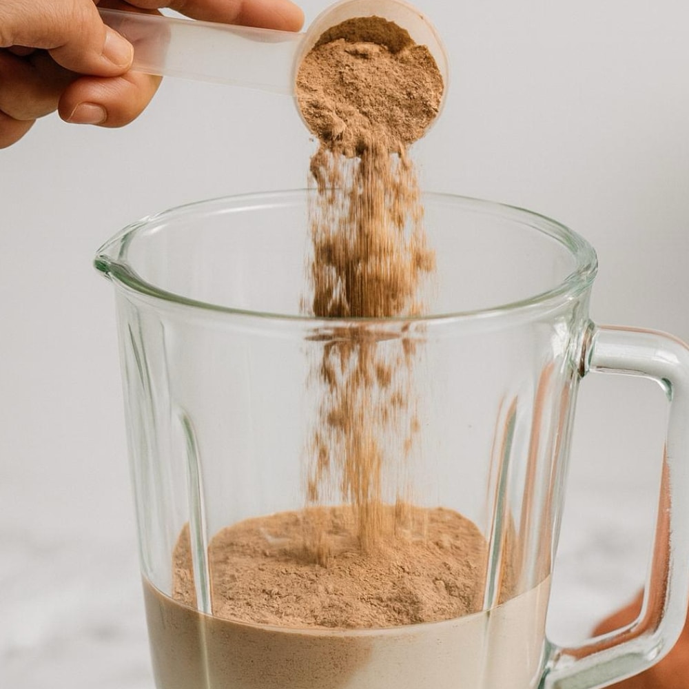 Pouring a scoop of cocoa-flavour Satislent into a blender jug with water