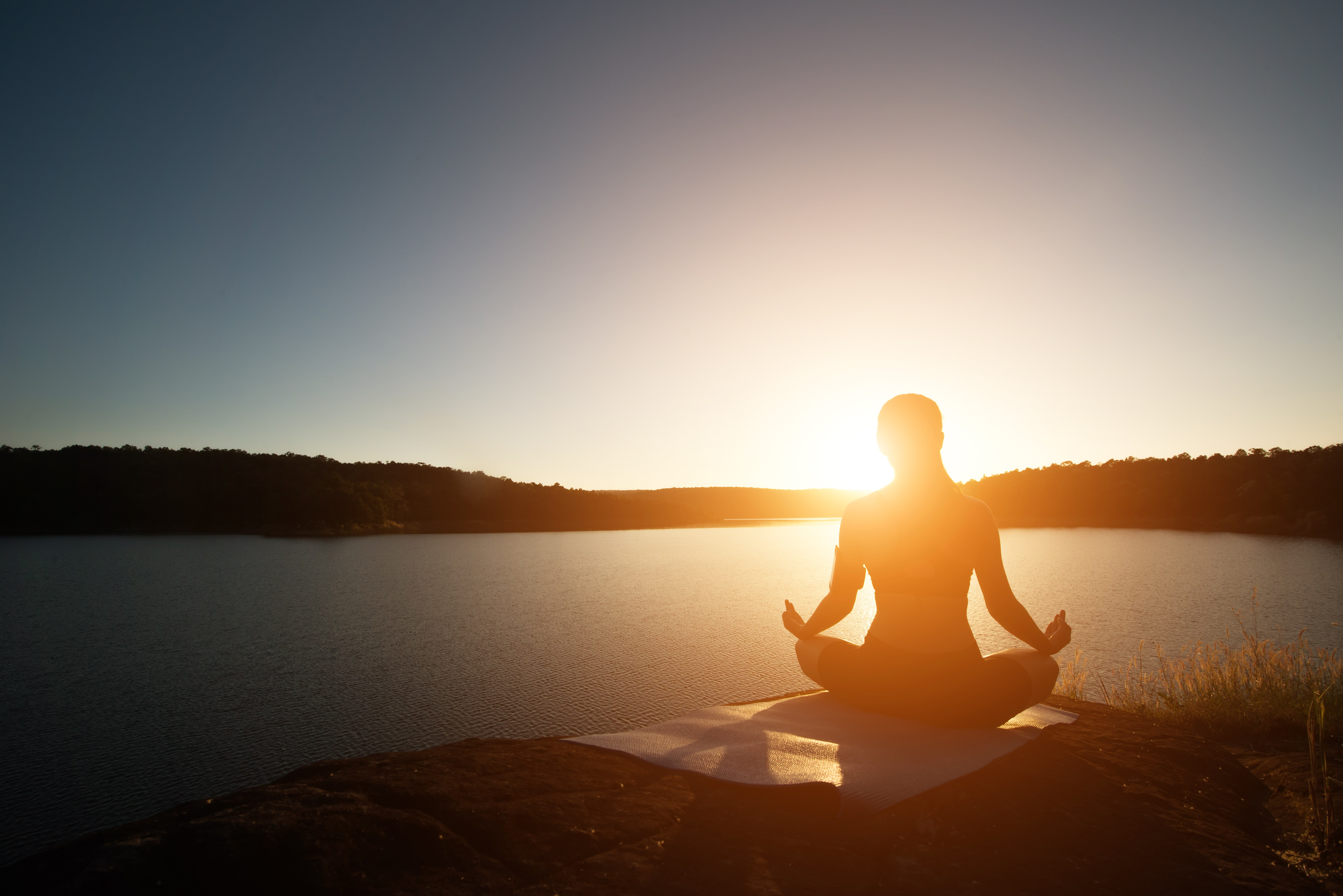 Personne m&eacute;ditant au lever du soleil devant un lac, repr&eacute;sentant la concentration et le calme dans le Monk Mode